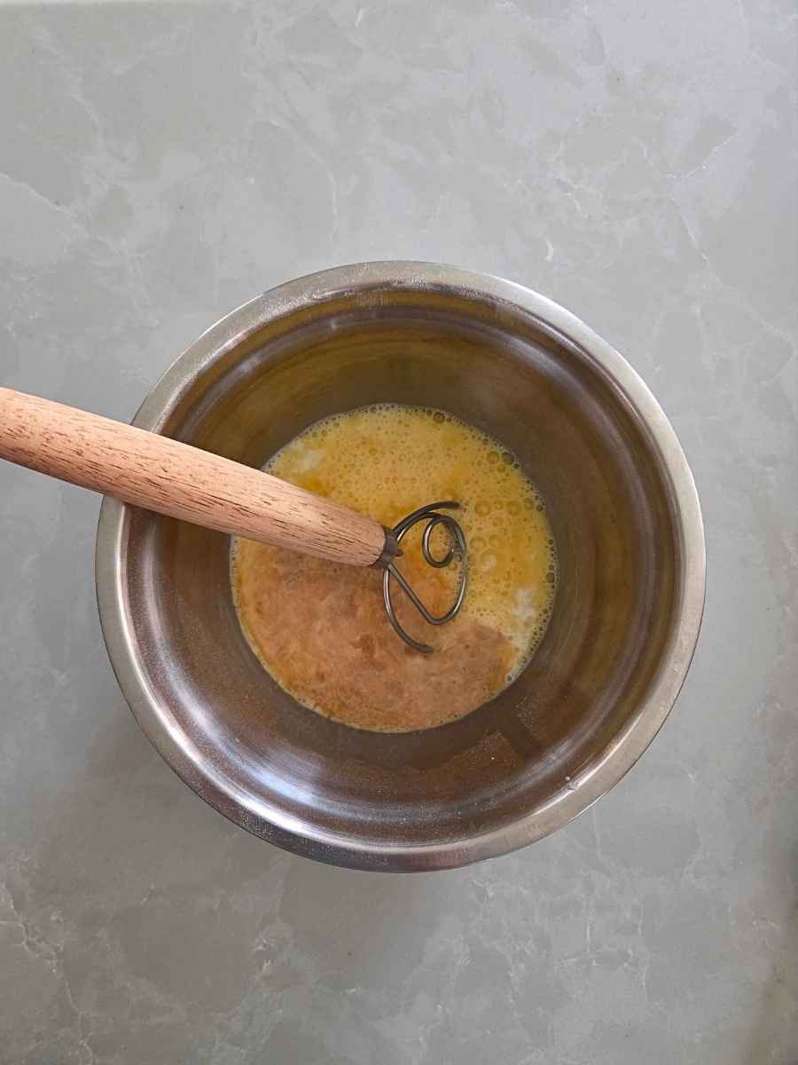 Eggs, vanilla, and milk whisked together in a stainless steel mixing bowl.