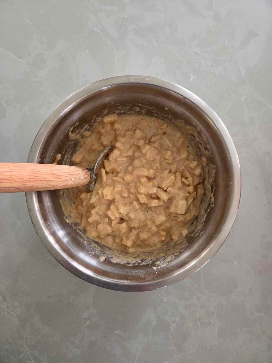 Thick, cinnamon-spiced pancake batter filled with diced apples in a mixing bowl.