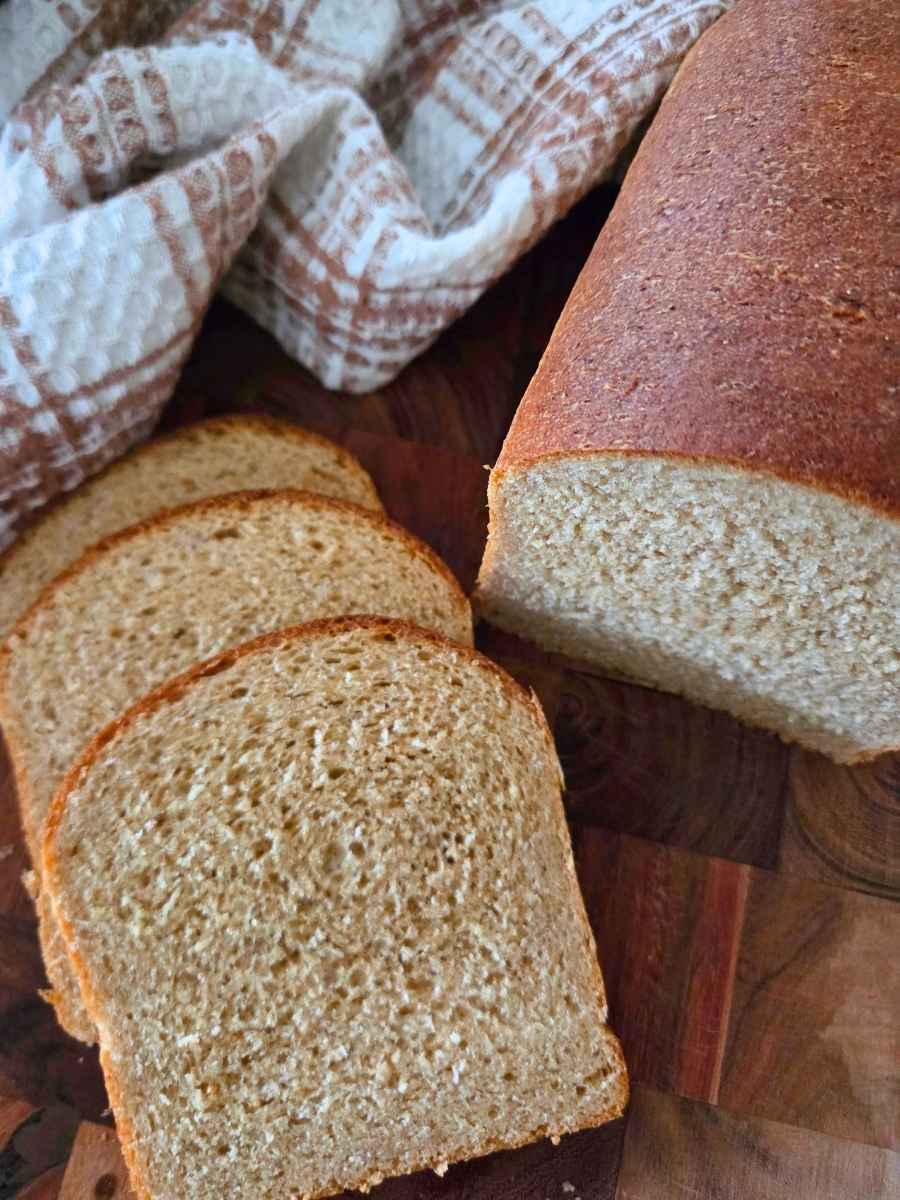 Sliced fresh milled flour sandwich bread made with vital wheat gluten, showing a soft, fine, and uniform crumb beside the remaining loaf.